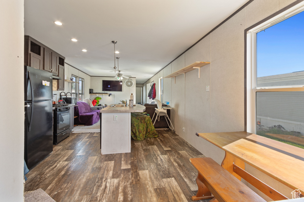 Kitchen with plenty of natural light, ceiling fan, black refrigerator, and dark wood-type flooring