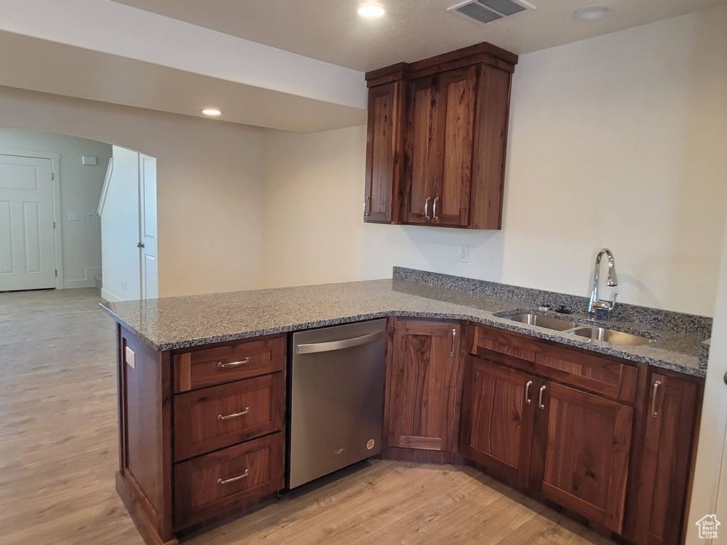 Kitchen with dark stone counters, sink, light hardwood / wood-style flooring, and stainless steel dishwasher