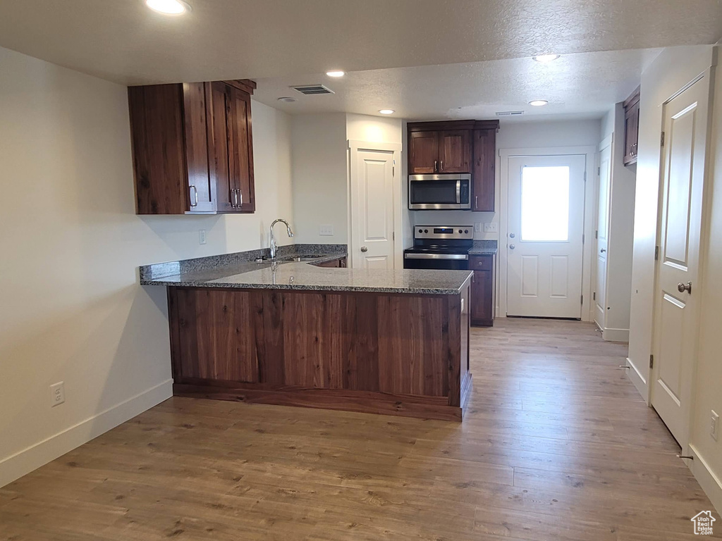 Kitchen with sink, stone counters, kitchen peninsula, and hardwood / wood-style flooring