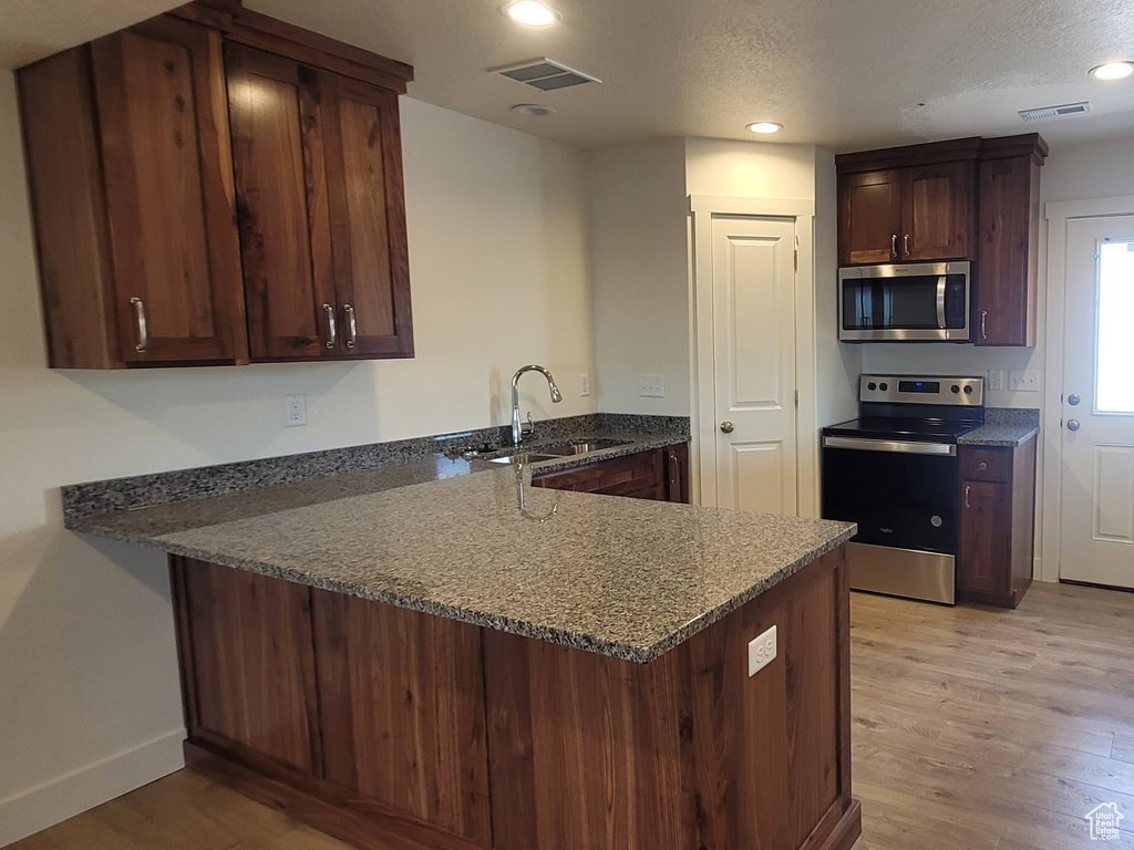 Kitchen with dark stone counters, kitchen peninsula, stainless steel appliances, light wood-type flooring, and sink