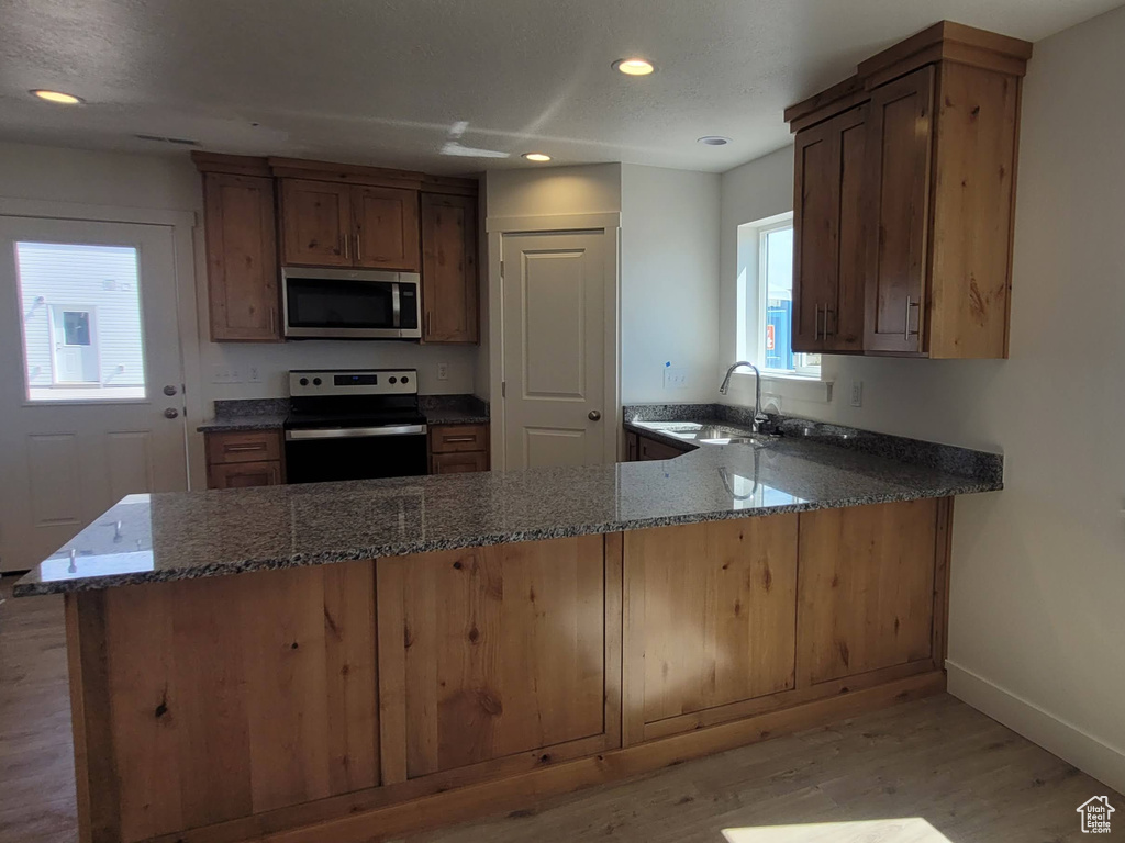 Kitchen with kitchen peninsula, light wood-type flooring, sink, stone countertops, and appliances with stainless steel finishes