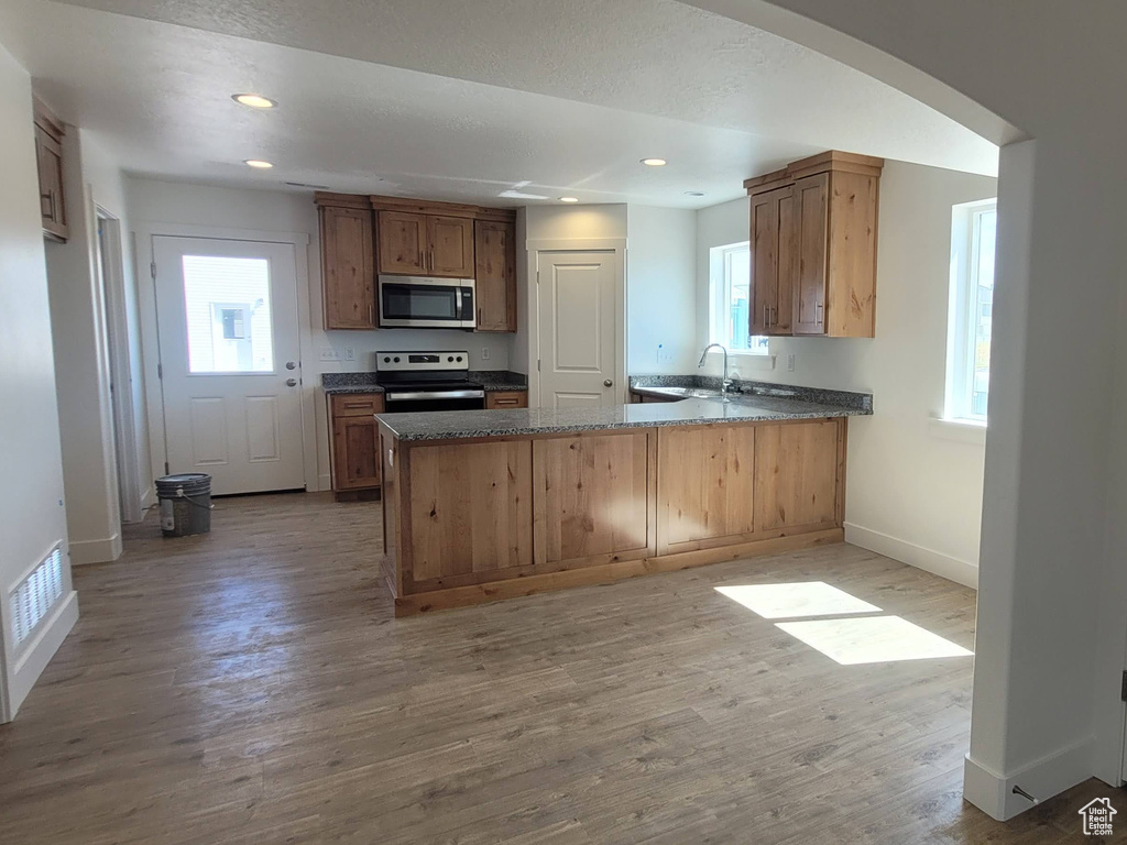 Kitchen with dark stone counters, light hardwood / wood-style flooring, kitchen peninsula, stainless steel appliances, and sink