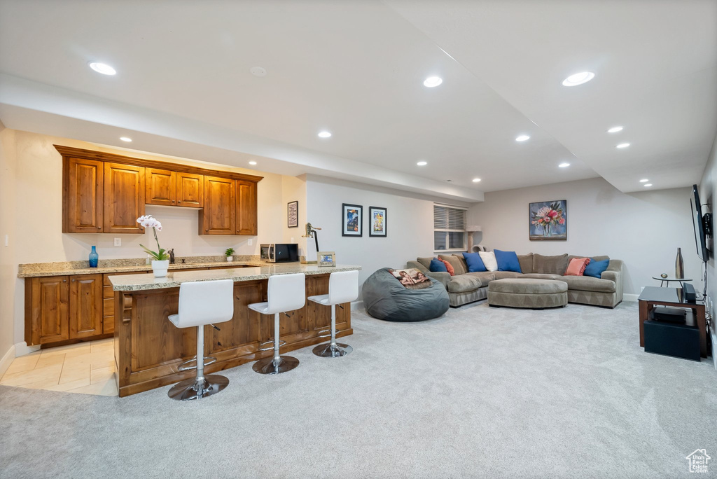 Kitchen with a kitchen island, a kitchen breakfast bar, light stone counters, and light colored carpet