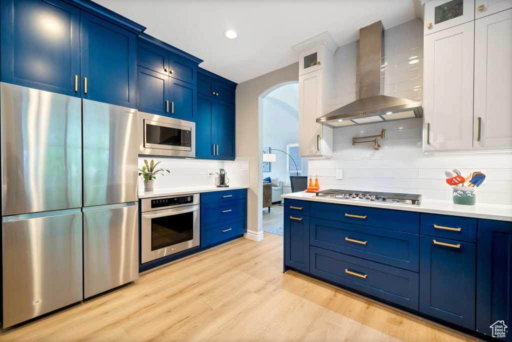 Kitchen featuring appliances with stainless steel finishes, tasteful backsplash, blue cabinetry, and wall chimney exhaust hood