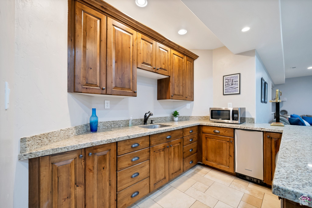 Kitchen with kitchen peninsula, stainless steel appliances, light stone countertops, sink, and light tile floors