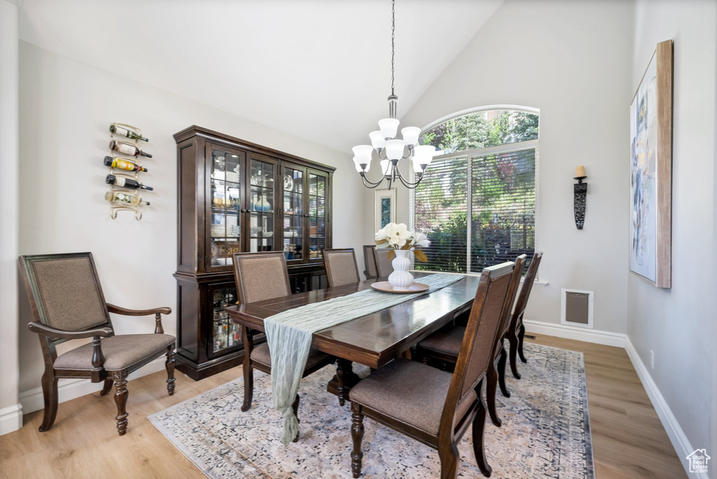 Dining area with a notable chandelier, high vaulted ceiling, and light wood-type flooring