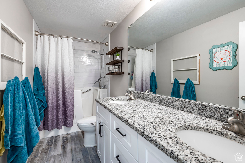 Full bathroom featuring hardwood / wood-style floors, dual vanity, shower / tub combo, a textured ceiling, and toilet