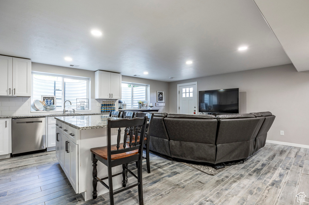 Kitchen featuring light stone counters, dishwasher, tasteful backsplash, white cabinetry, and light wood-type flooring