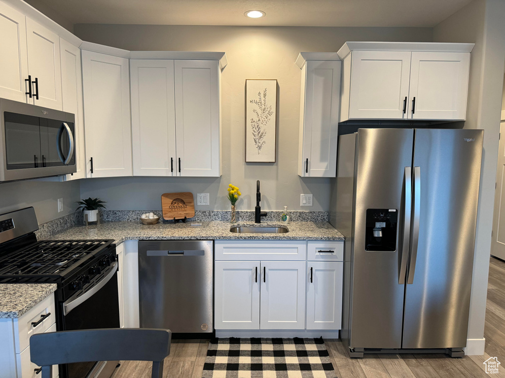 Kitchen with light stone countertops, light wood-type flooring, stainless steel appliances, white cabinets, and sink