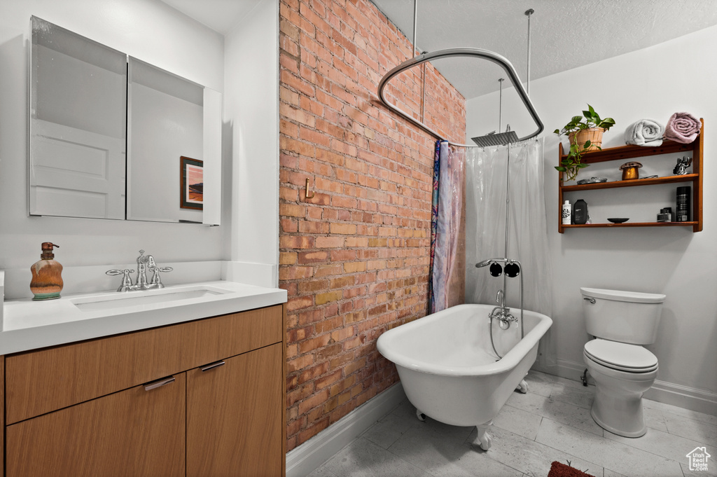 Bathroom with tile flooring, brick wall, a textured ceiling, vanity, and toilet