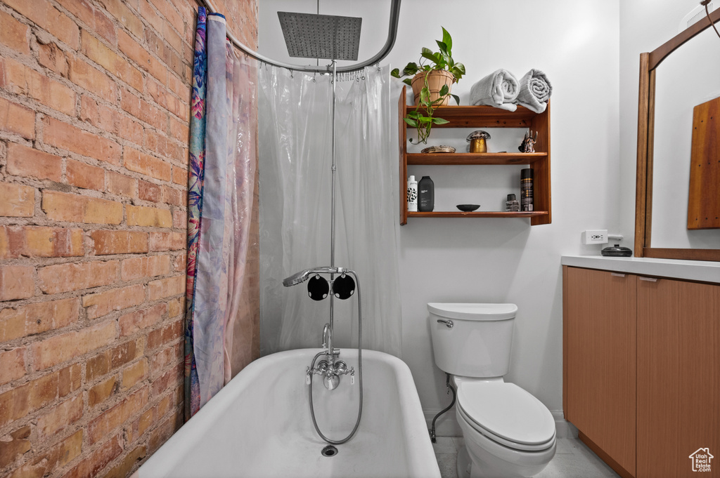 Bathroom featuring brick wall, vanity, toilet, and tile floors