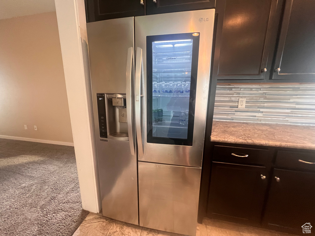 Room details with backsplash, stainless steel fridge, dark brown cabinetry, and light colored carpet