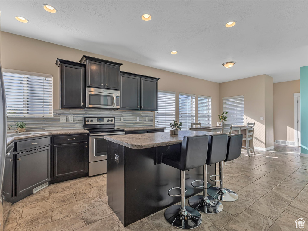 Kitchen featuring a kitchen island, appliances with stainless steel finishes, backsplash, a breakfast bar, and light tile floors
