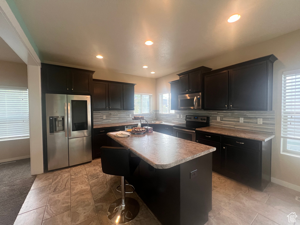 Kitchen with a kitchen island, backsplash, a kitchen bar, appliances with stainless steel finishes, and light tile floors