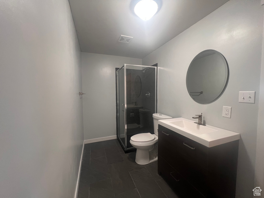 Bathroom with a shower with door, tile flooring, vanity with extensive cabinet space, and toilet