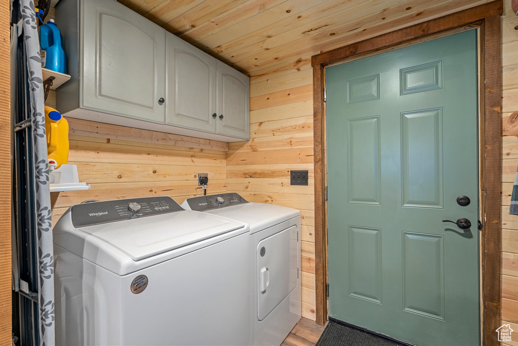 Clothes washing area with cabinets, light hardwood / wood-style flooring, hookup for an electric dryer, independent washer and dryer, and wood walls