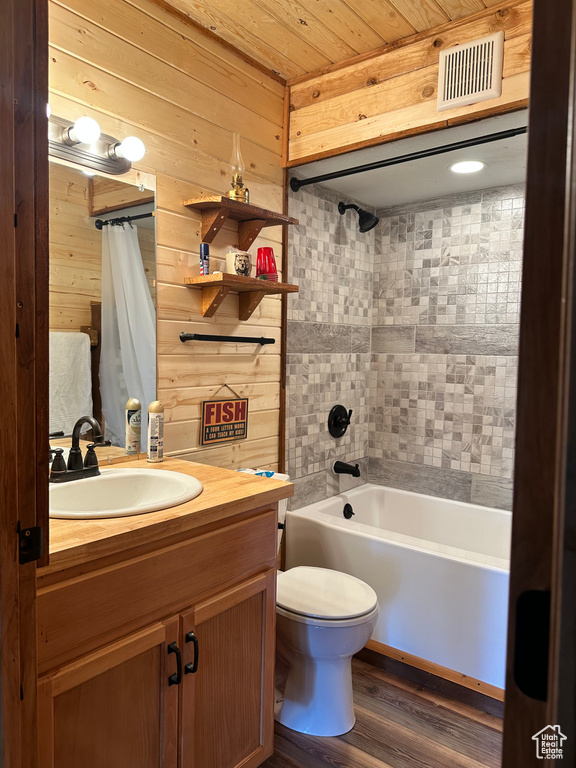 Full bathroom with hardwood / wood-style flooring, wooden walls, shower / bath combination with curtain, vanity, and toilet
