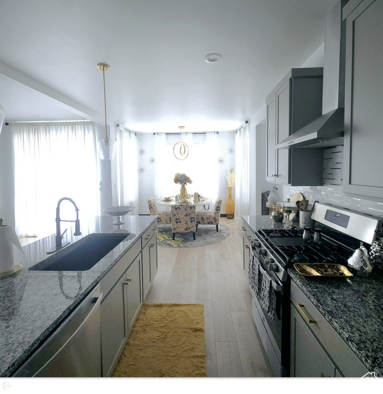 Kitchen with wall chimney range hood, light hardwood / wood-style floors, stainless steel appliances, gray cabinets, and sink