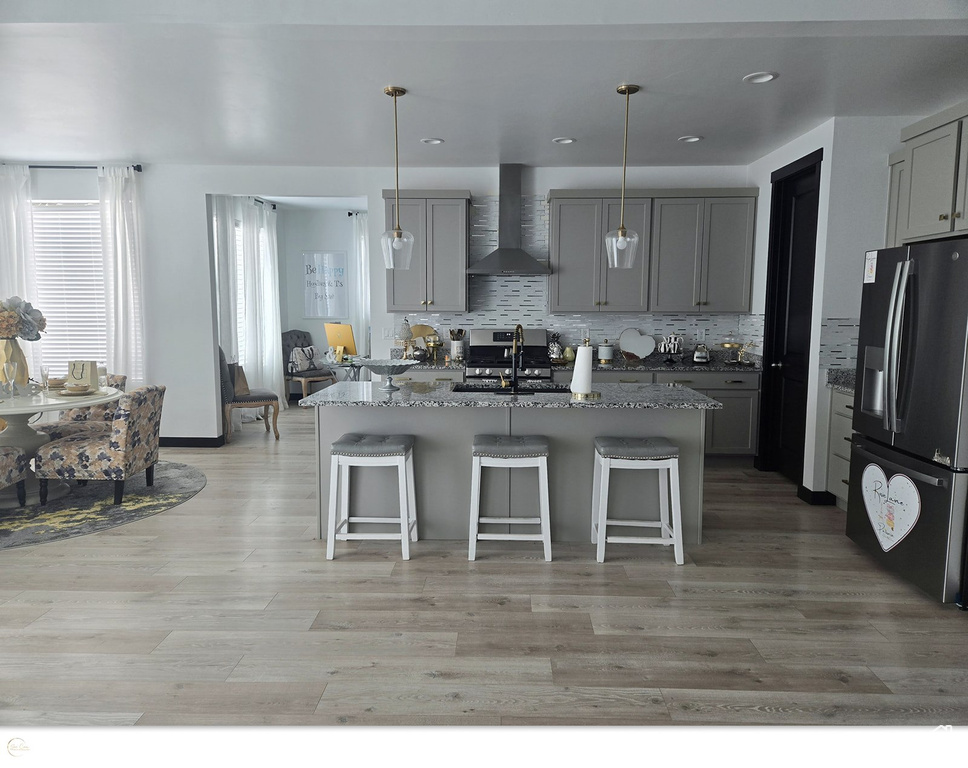 Kitchen featuring stainless steel appliances, dark stone countertops, wall chimney exhaust hood, and decorative light fixtures