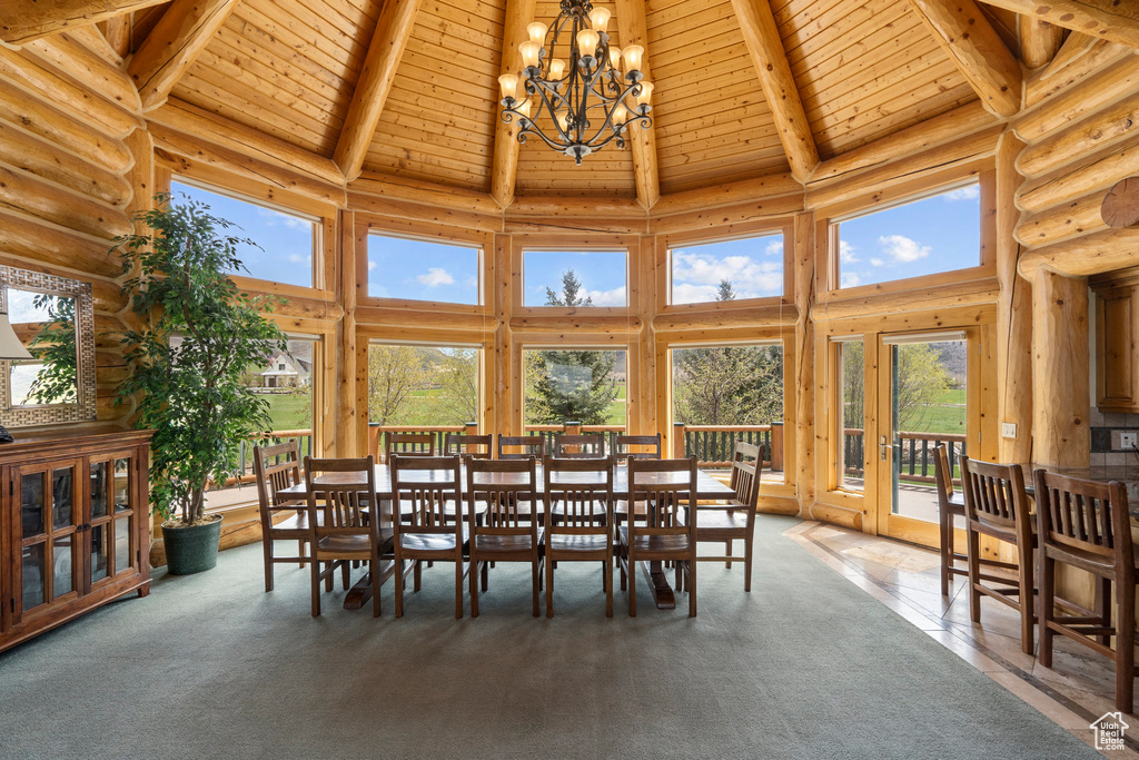 Carpeted dining space with high vaulted ceiling, an inviting chandelier, log walls, and wooden ceiling