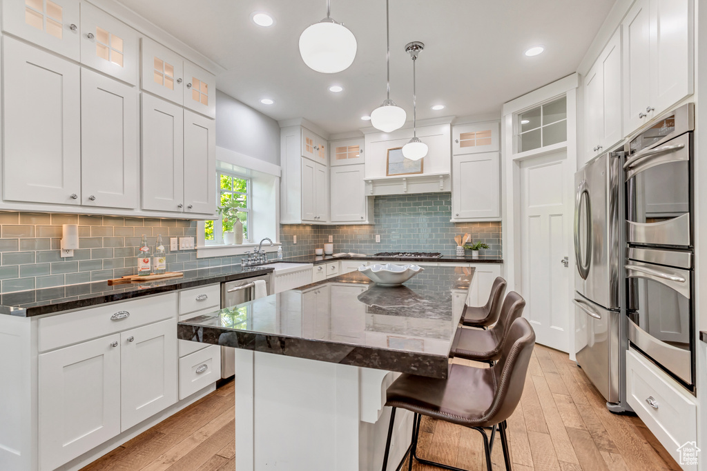 Kitchen with stainless steel appliances, light wood-type flooring, backsplash, a kitchen island, and white cabinetry