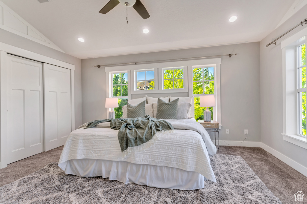 Carpeted bedroom with vaulted ceiling, a closet, ceiling fan, and multiple windows