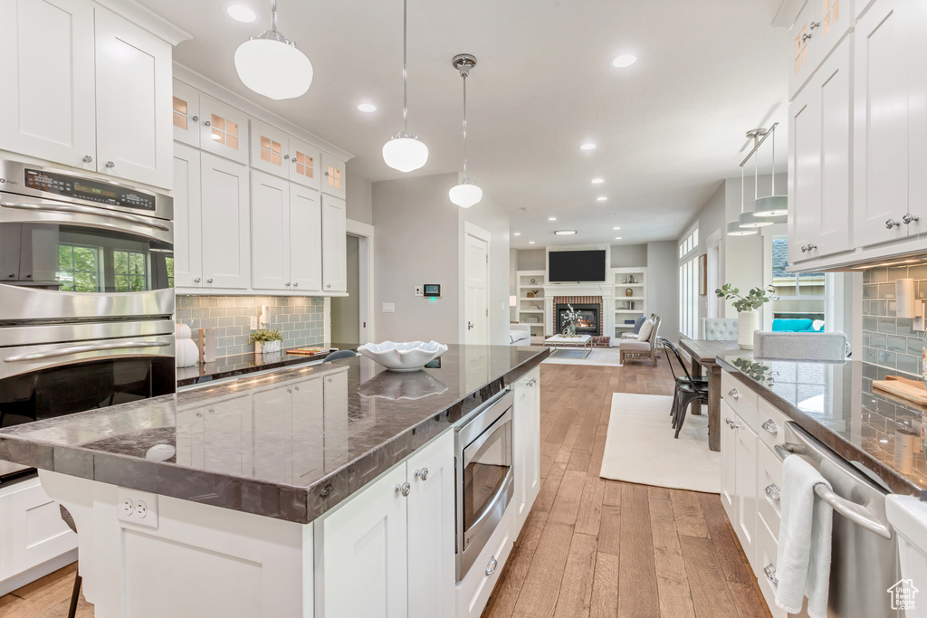 Kitchen featuring a center island, light wood-type flooring, appliances with stainless steel finishes, white cabinets, and backsplash