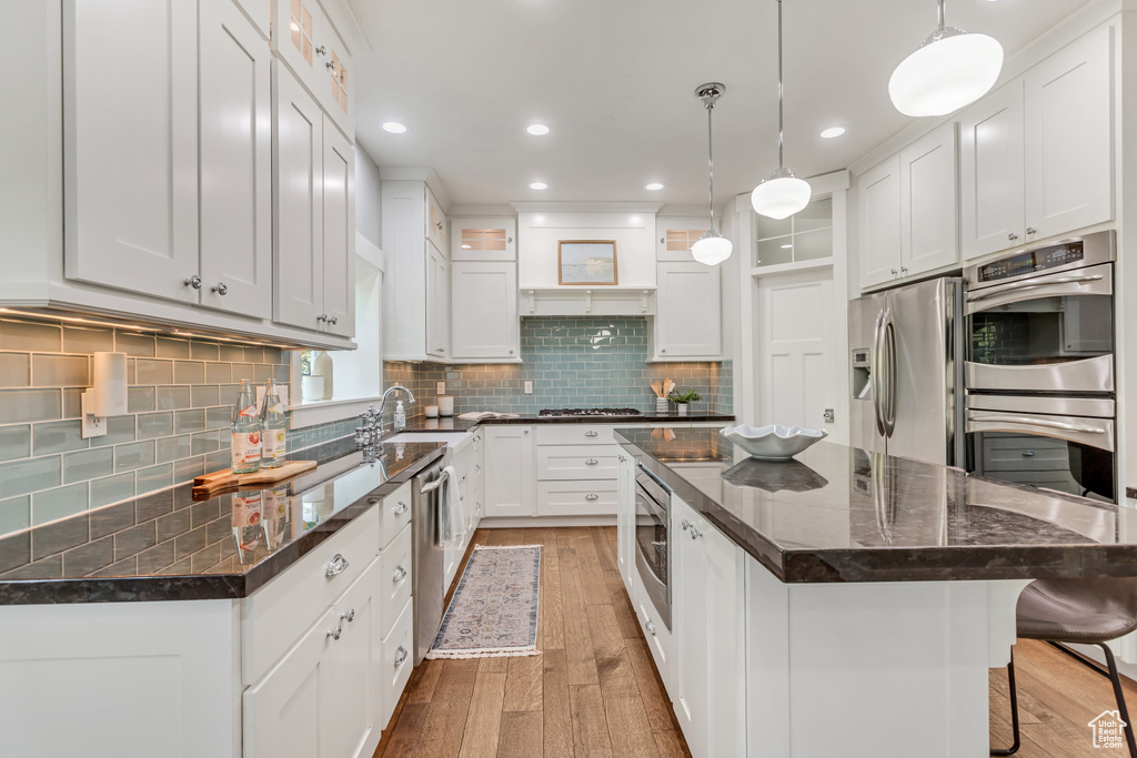 Kitchen featuring white cabinets, appliances with stainless steel finishes, tasteful backsplash, and a kitchen island