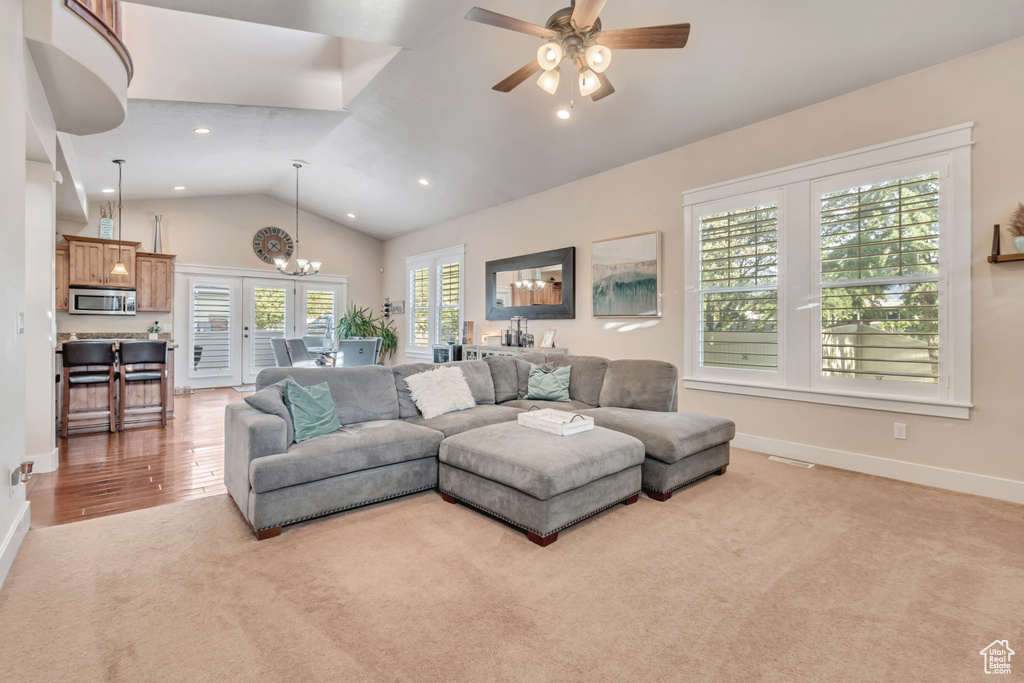 Carpeted living room featuring ceiling fan with notable chandelier, vaulted ceiling, and french doors