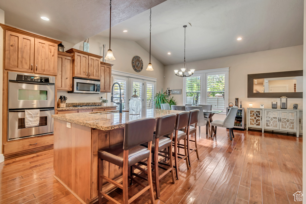 Kitchen featuring light hardwood / wood-style floors, hanging light fixtures, a center island with sink, stainless steel appliances, and a chandelier