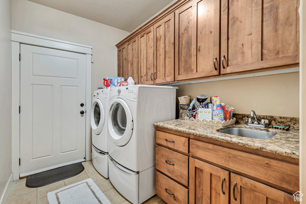 Clothes washing area featuring sink, washer and dryer, light tile flooring, and cabinets