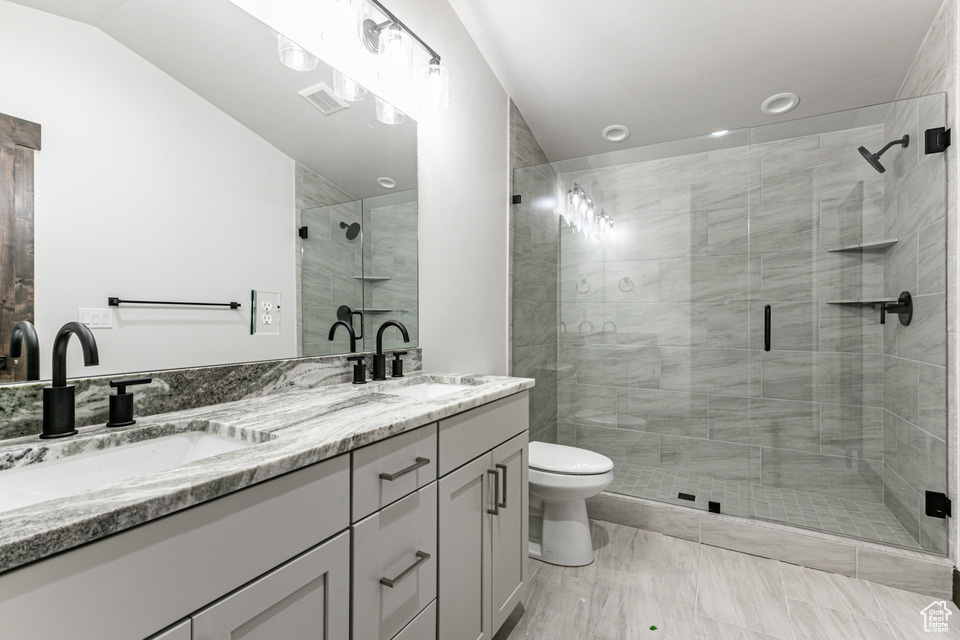 Bathroom featuring a shower with door, dual sinks, vanity with extensive cabinet space, and toilet