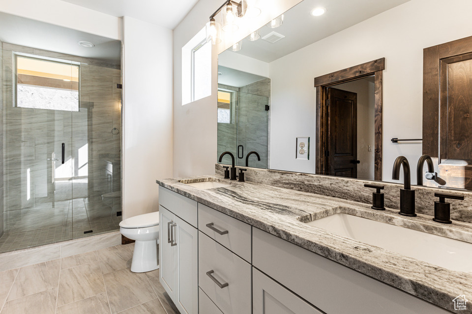 Bathroom featuring dual vanity, a shower with door, tile floors, and toilet