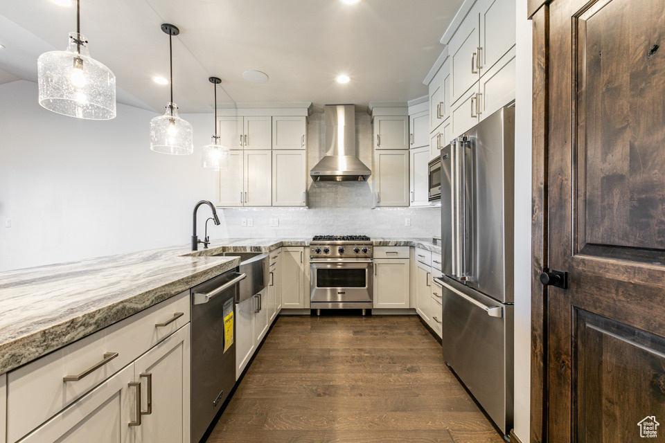 Kitchen with dark hardwood / wood-style floors, light stone countertops, pendant lighting, premium appliances, and wall chimney exhaust hood