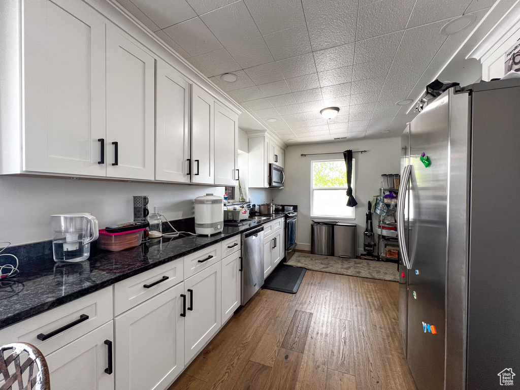 Kitchen with dark stone counters, white cabinets, hardwood / wood-style floors, and stainless steel appliances