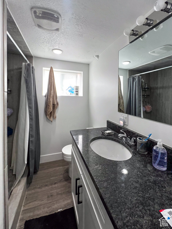 Bathroom featuring vanity with extensive cabinet space, a textured ceiling, toilet, and hardwood / wood-style floors