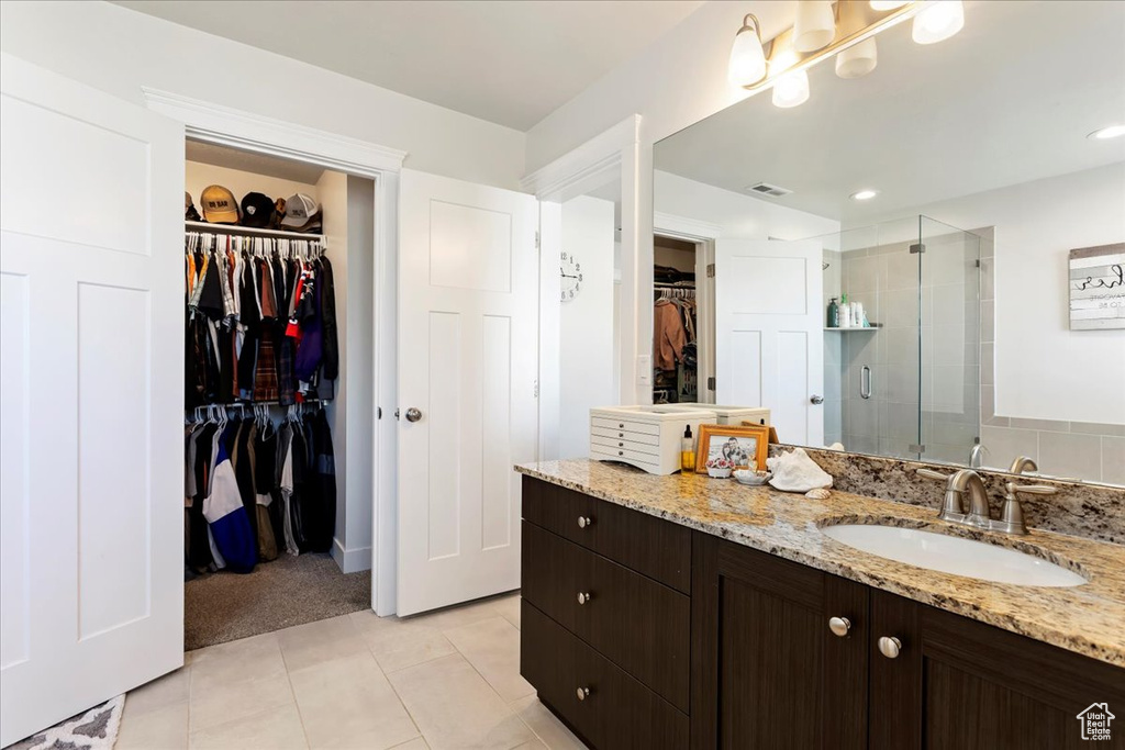 Bathroom featuring vanity with extensive cabinet space, tile floors, and a shower with door