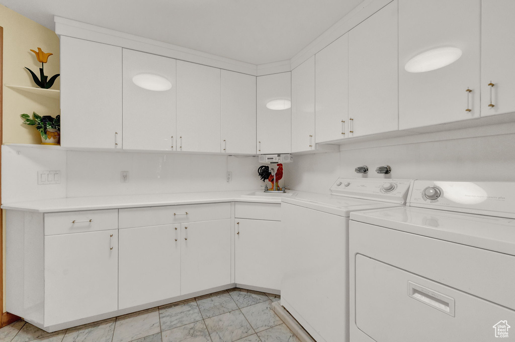 Clothes washing area with washer and dryer, cabinets, and light tile floors