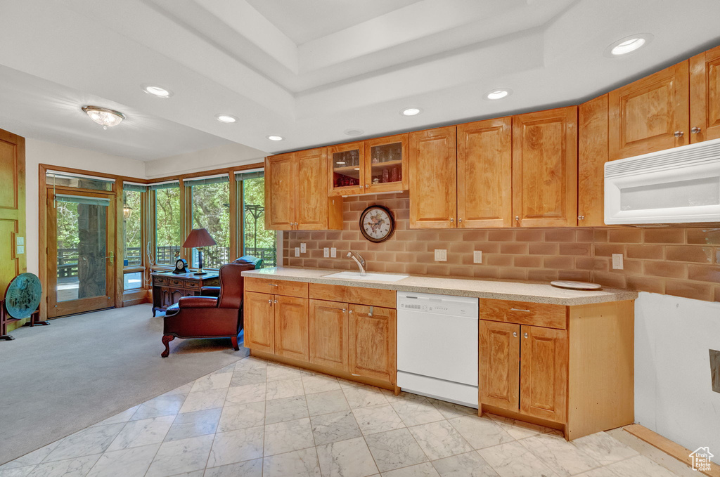 Kitchen with a tray ceiling, white appliances, backsplash, sink, and light colored carpet