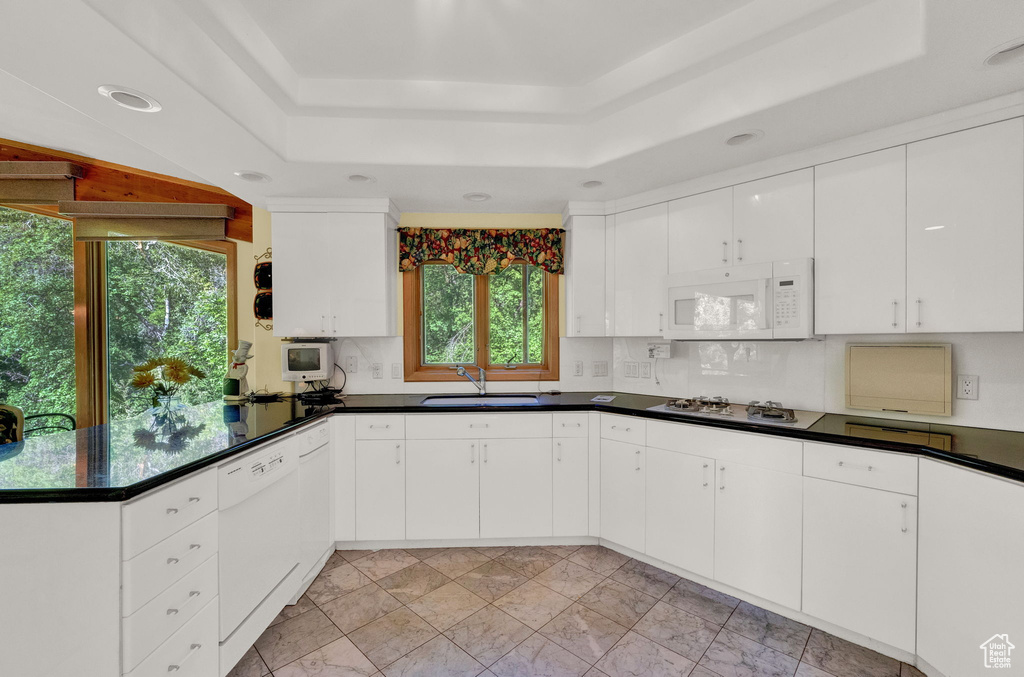 Kitchen with light tile flooring, a raised ceiling, white cabinets, sink, and white appliances