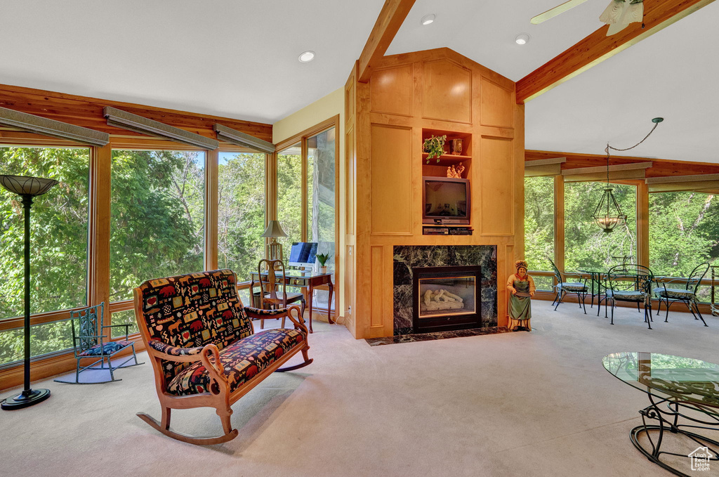 Living room featuring ceiling fan, vaulted ceiling with beams, a high end fireplace, and light colored carpet