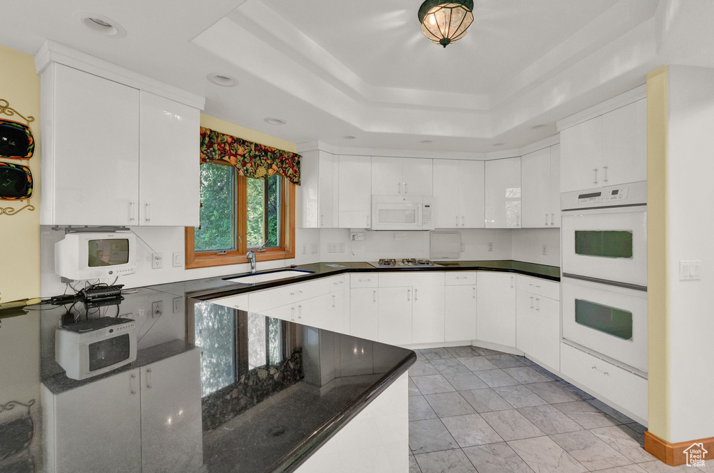 Kitchen featuring white appliances, sink, light tile flooring, and a raised ceiling