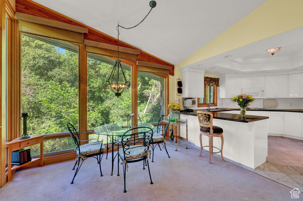 Carpeted dining room with a tray ceiling, a healthy amount of sunlight, lofted ceiling, and an inviting chandelier