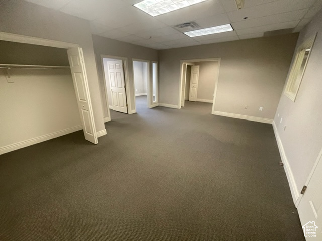 Unfurnished bedroom with a paneled ceiling, a closet, and dark colored carpet