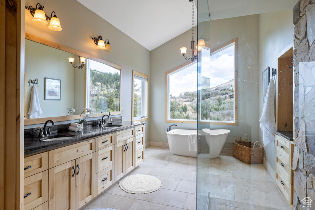 Bathroom featuring an inviting chandelier, a bathing tub, dual bowl vanity, tile flooring, and lofted ceiling