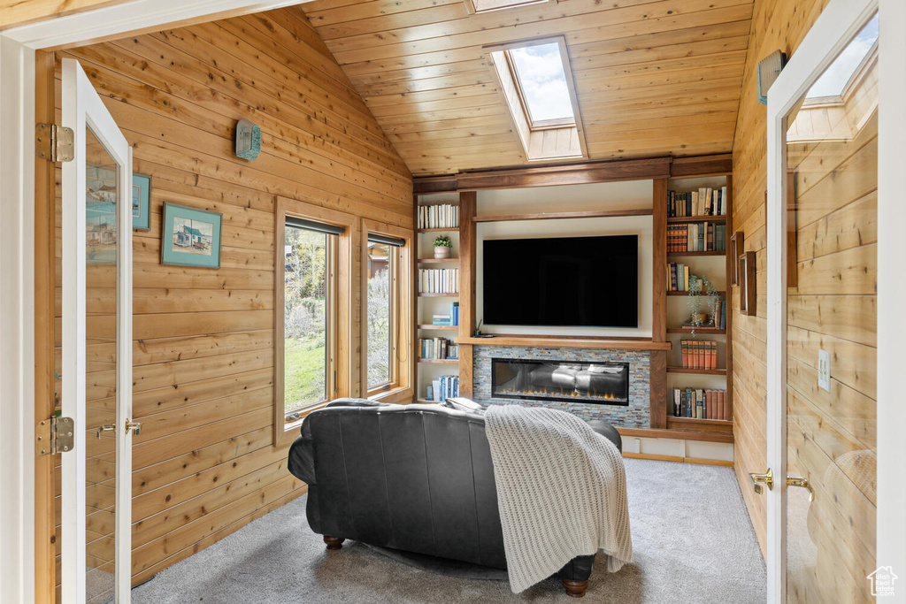 Carpeted living room with french doors, vaulted ceiling with skylight, a fireplace, wood ceiling, and wood walls