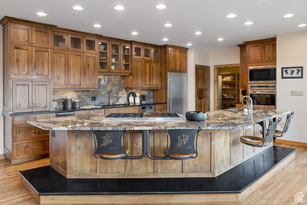 Kitchen with light hardwood / wood-style floors, stainless steel appliances, stone counters, a large island, and a breakfast bar