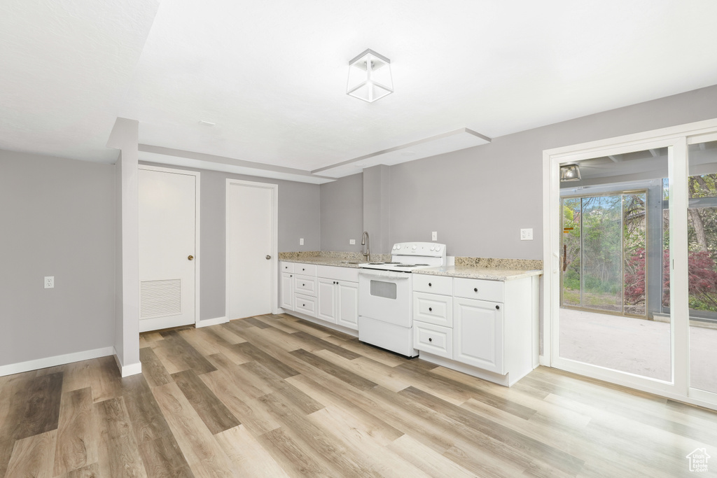 Kitchen featuring light wood-type flooring, white range with electric cooktop, light stone counters, sink, and white cabinets