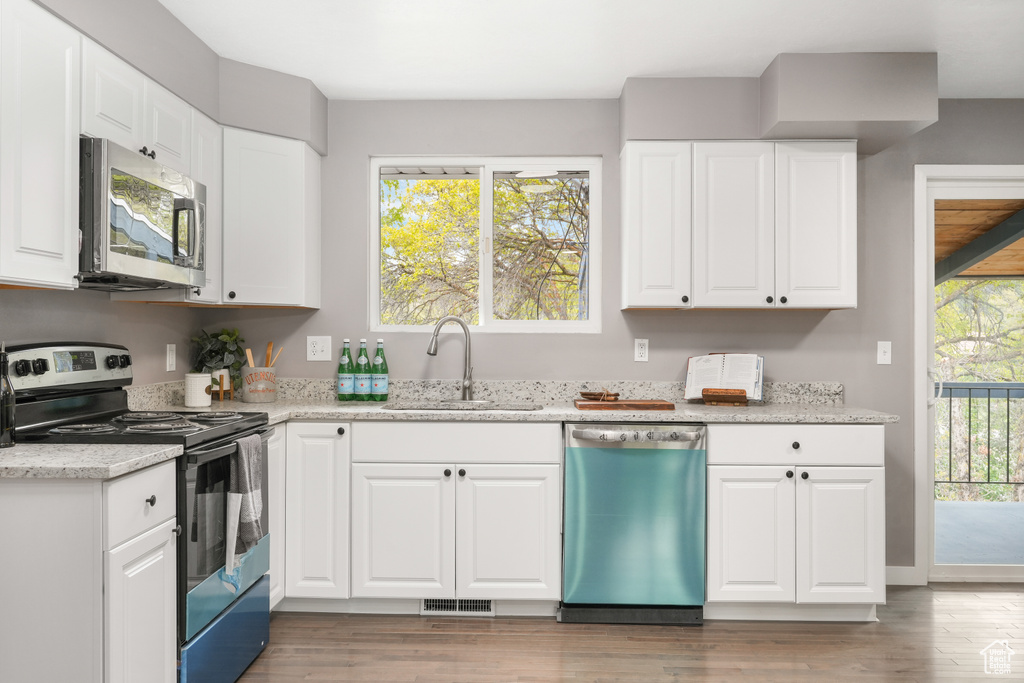 Kitchen with hardwood / wood-style floors, white cabinetry, light stone countertops, appliances with stainless steel finishes, and sink