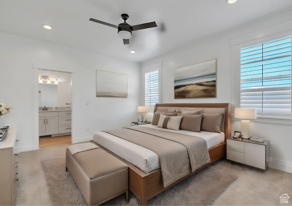 Bedroom with light carpet, ceiling fan, multiple windows, and ensuite bath